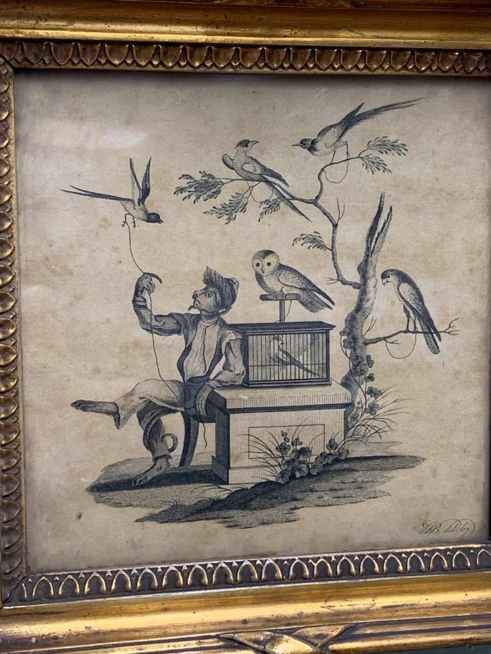 An 18th-century monochrome etching featuring a clothed monkey seated beside a birdcage surrounded by birds, enclosed in an ornate gold leaf frame. View IV
