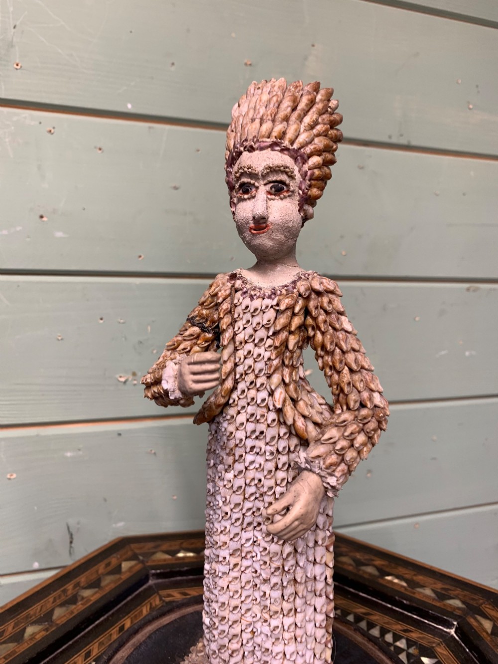 A standing figure of a woman sculpted from tiny arranged seashells on a circular dark wood base. View III