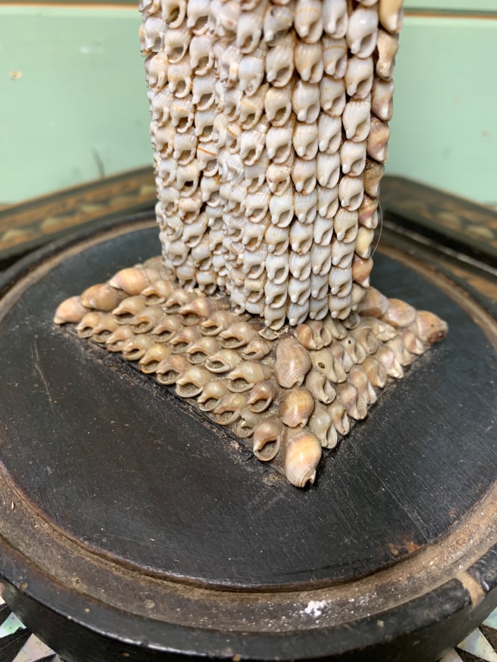 A standing figure of a woman sculpted from tiny arranged seashells on a circular dark wood base. View IV