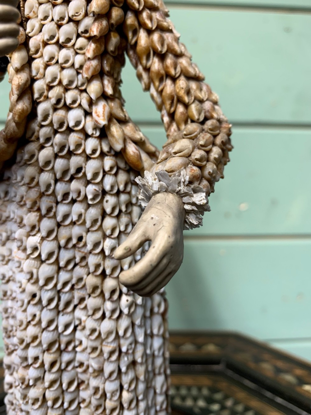 A standing figure of a woman sculpted from tiny arranged seashells on a circular dark wood base. View VI