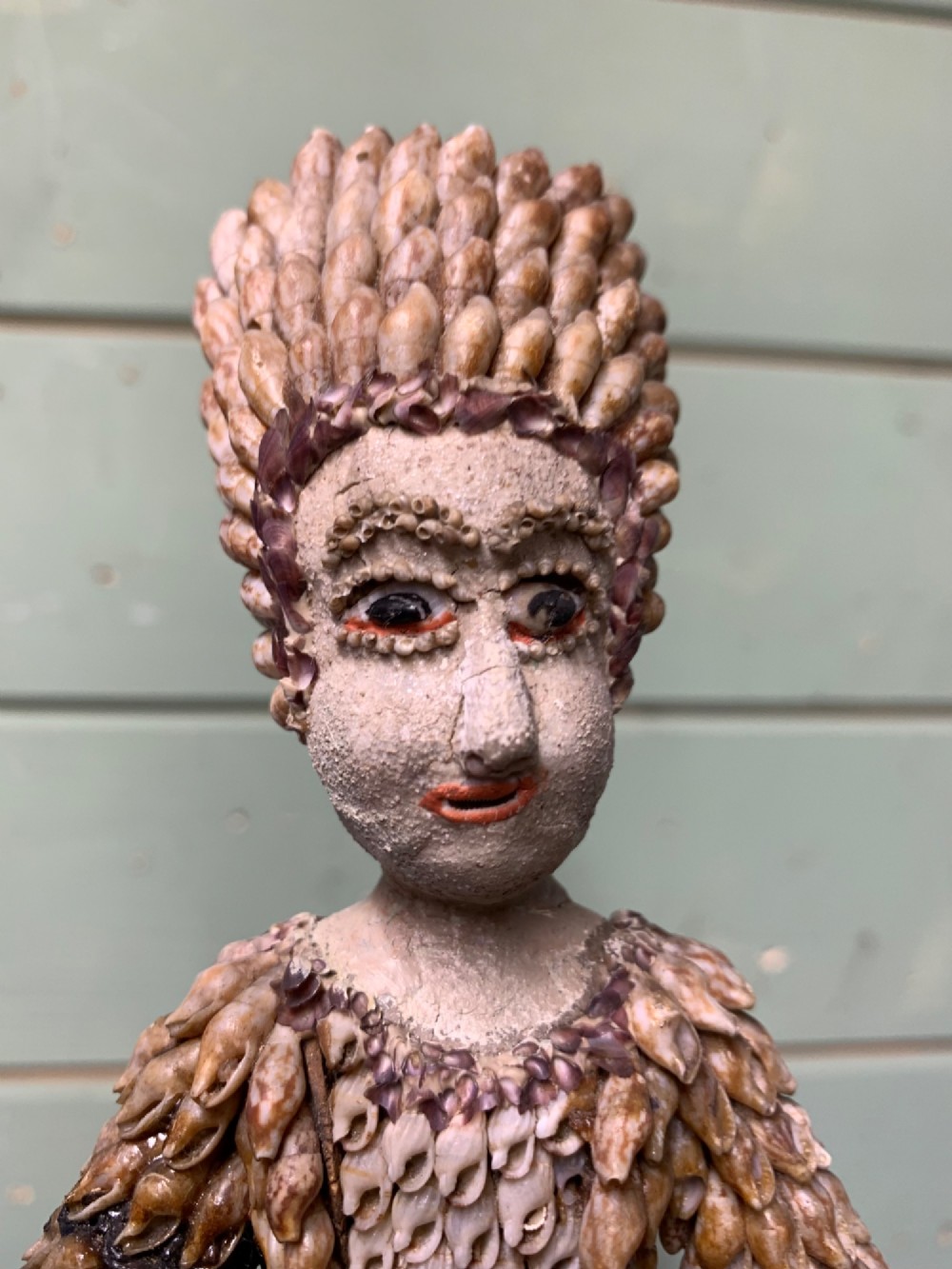 A standing figure of a woman sculpted from tiny arranged seashells on a circular dark wood base. View VII