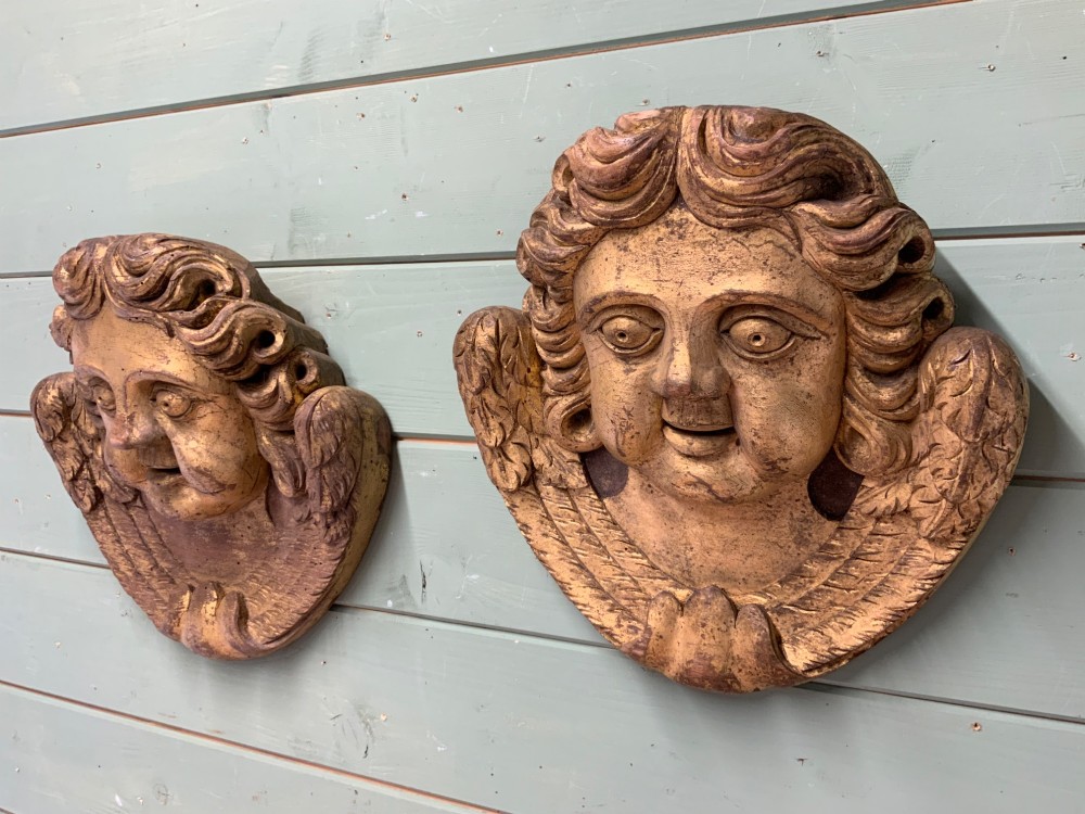 A pair of French carved wooden church angel heads featuring curly hair and sculpted wings framing the face with remnants of gilded paint. View III