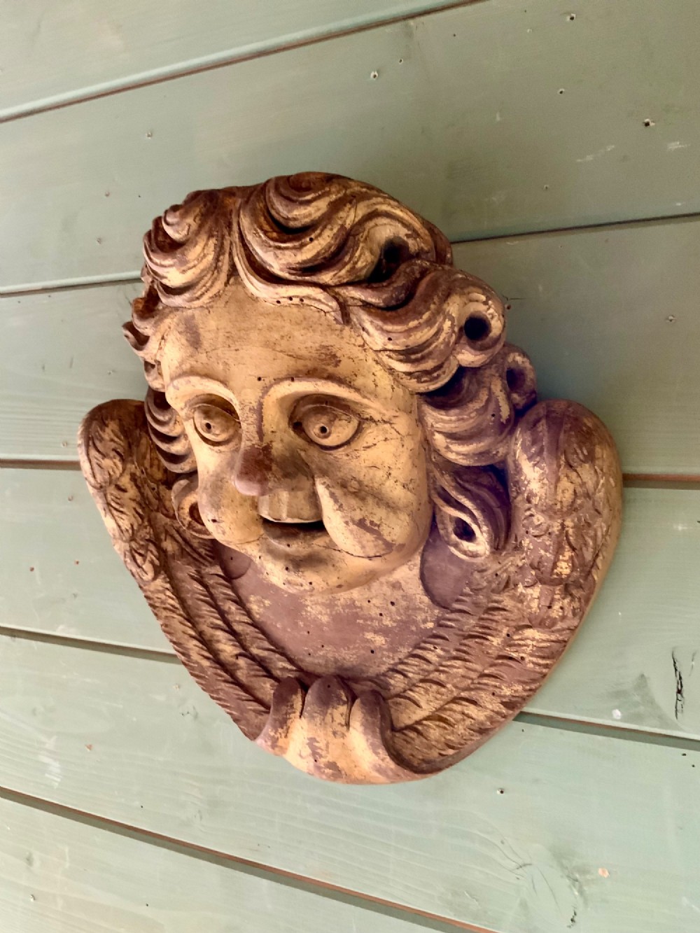 A pair of French carved wooden church angel heads featuring curly hair and sculpted wings framing the face with remnants of gilded paint. View V
