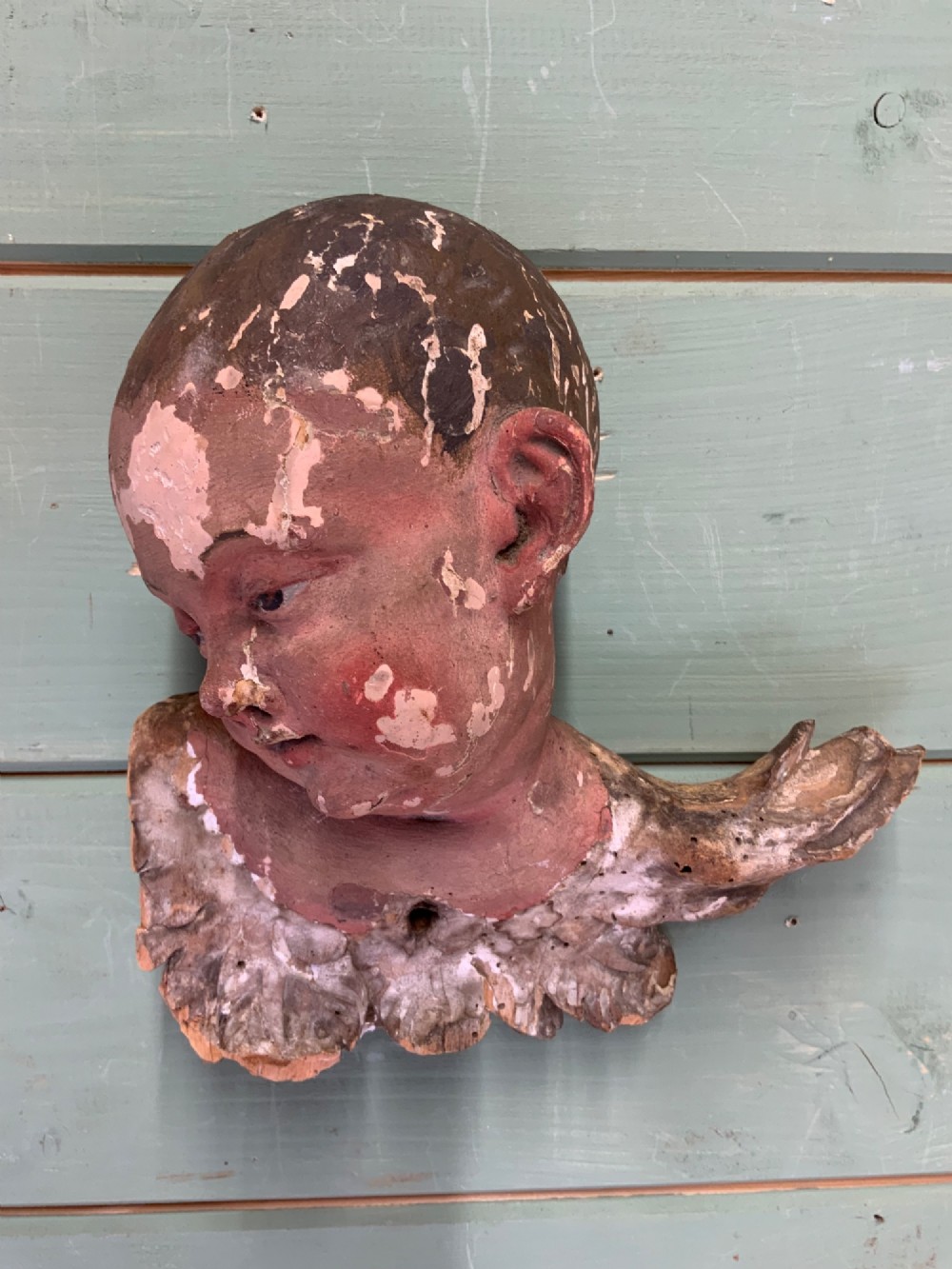 An early 18th-century carved wooden putto head featuring distressed polychrome paint and stylized winged detailing. View III