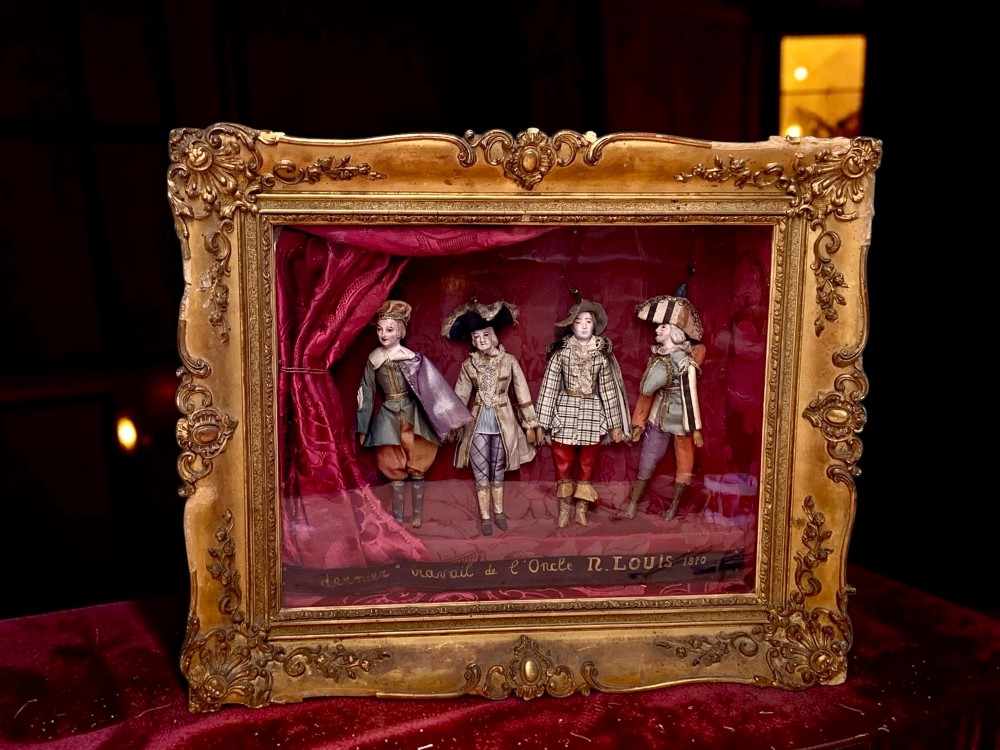 An antique gilt-framed shadow box diorama depicting four miniature costumed theatrical figures against a crimson draped fabric backdrop.
