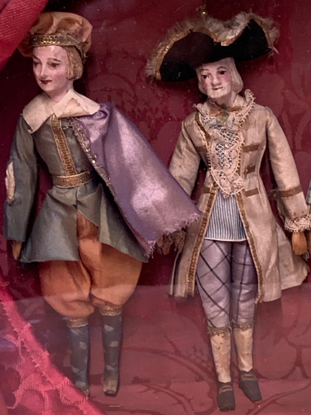 An antique gilt-framed shadow box diorama depicting four miniature costumed theatrical figures against a crimson draped fabric backdrop. View VI