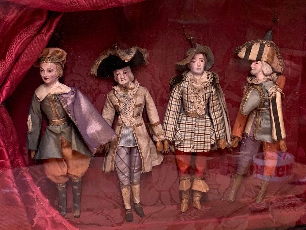 An antique gilt-framed shadow box diorama depicting four miniature costumed theatrical figures against a crimson draped fabric backdrop. View VIII