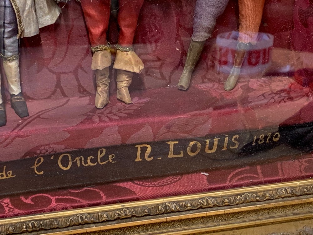 An antique gilt-framed shadow box diorama depicting four miniature costumed theatrical figures against a crimson draped fabric backdrop. View IX