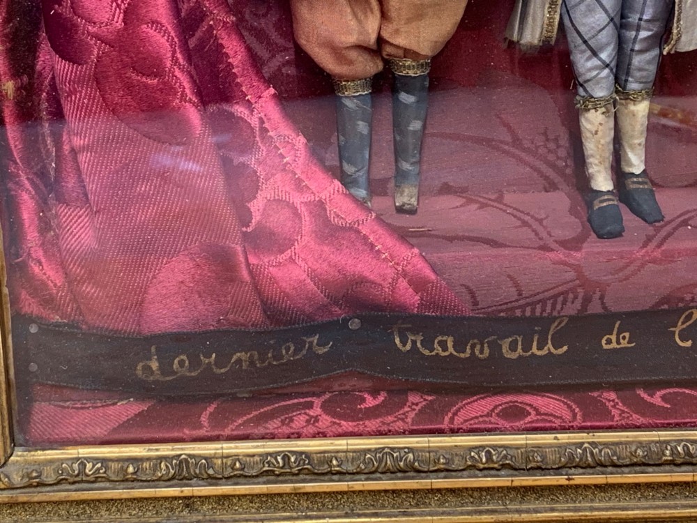 An antique gilt-framed shadow box diorama depicting four miniature costumed theatrical figures against a crimson draped fabric backdrop. View X