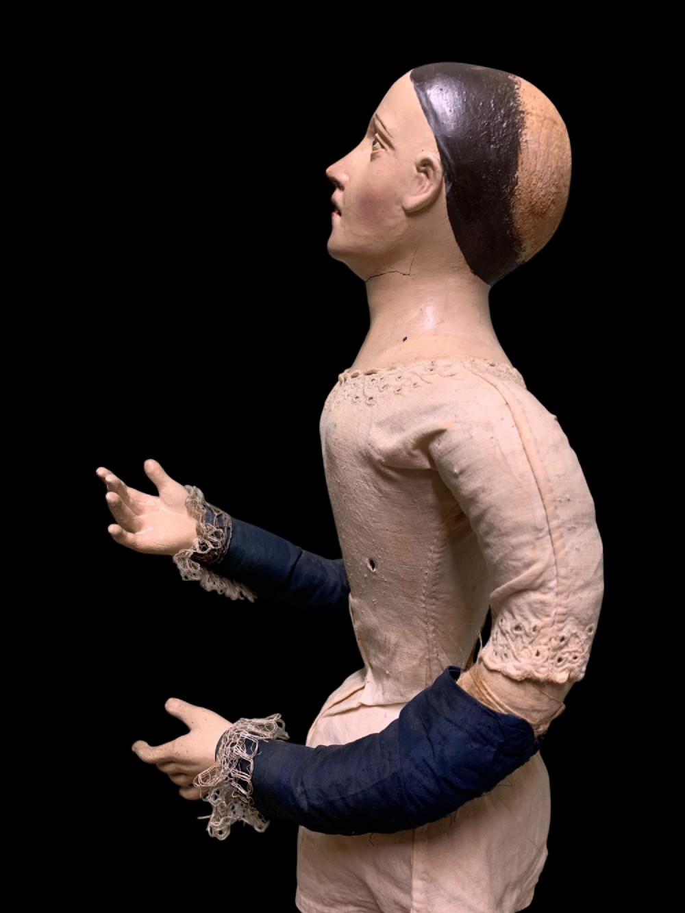 A 19th-century processional mannequin with carved polychrome head and hands, dressed in cream fabric with dark blue sleeves, standing on a four-legged wooden cage base. View III