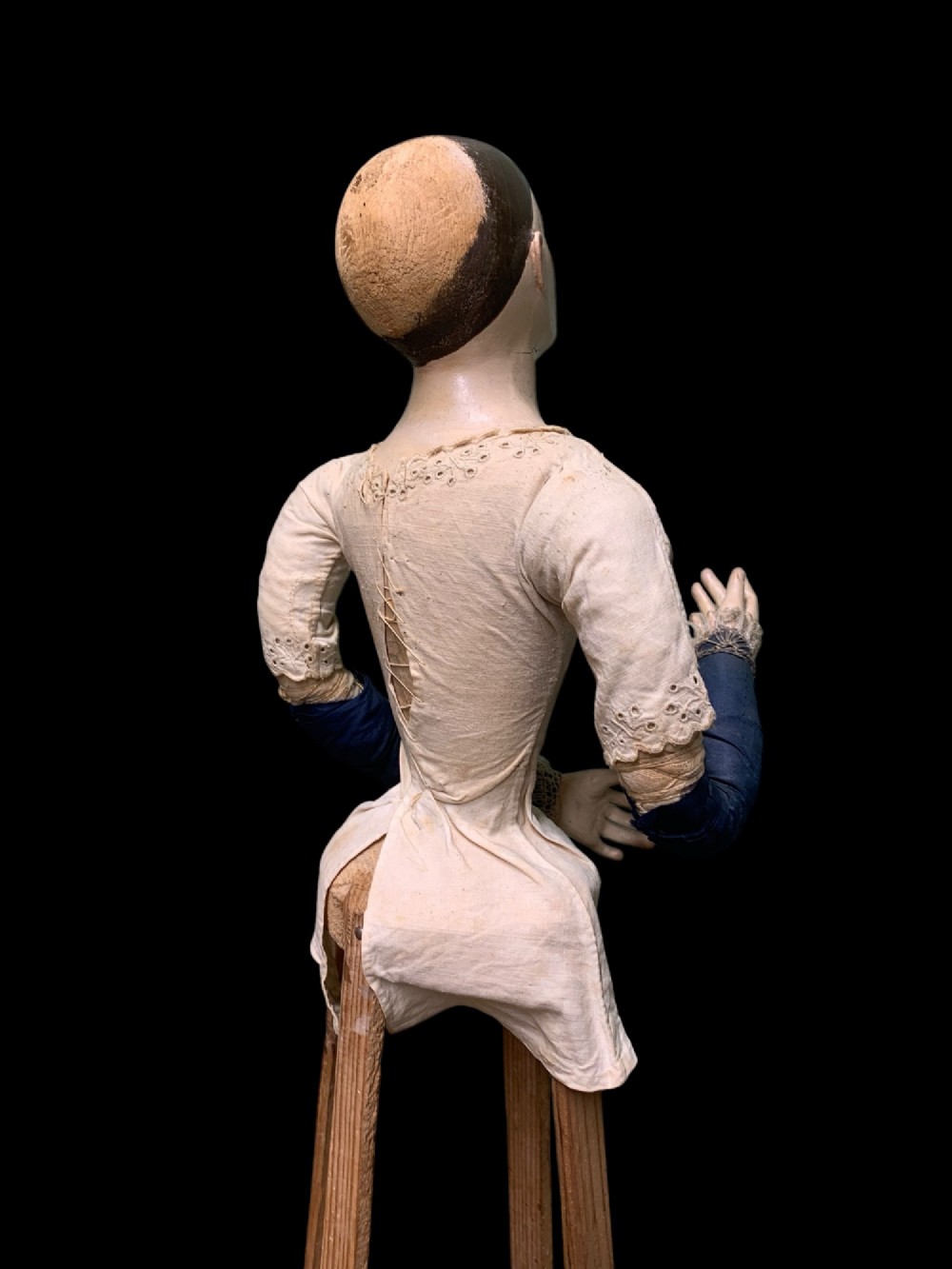 A 19th-century processional mannequin with carved polychrome head and hands, dressed in cream fabric with dark blue sleeves, standing on a four-legged wooden cage base. View V
