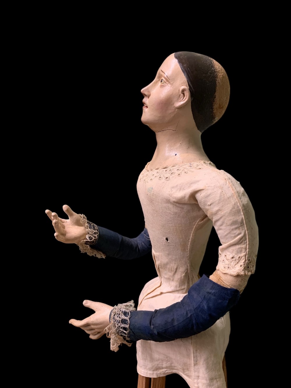 A 19th-century processional mannequin with carved polychrome head and hands, dressed in cream fabric with dark blue sleeves, standing on a four-legged wooden cage base. View VIII