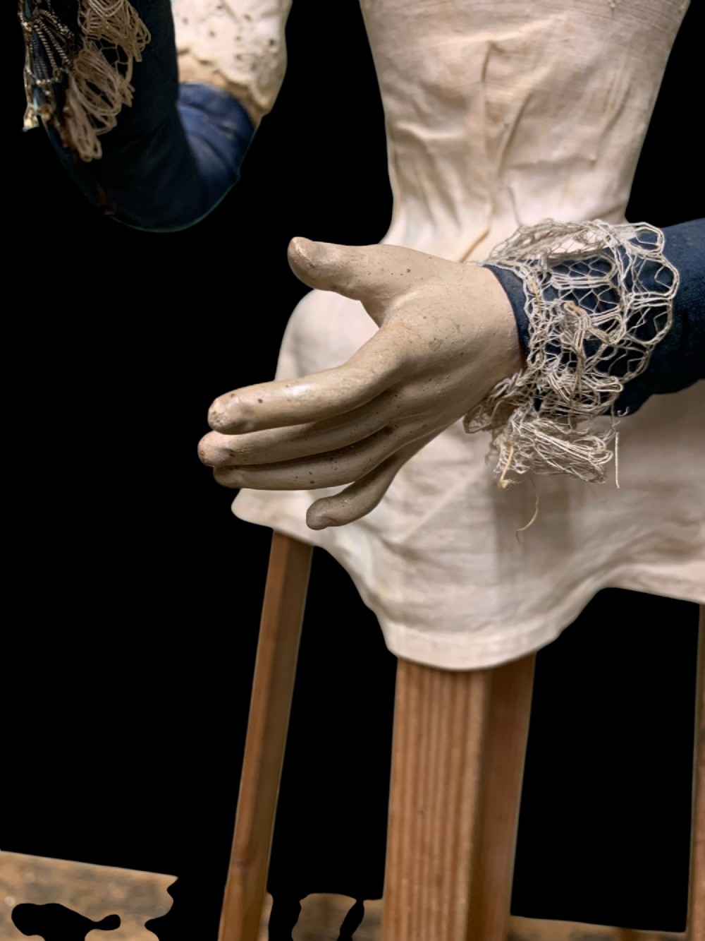 A 19th-century processional mannequin with carved polychrome head and hands, dressed in cream fabric with dark blue sleeves, standing on a four-legged wooden cage base. View XI