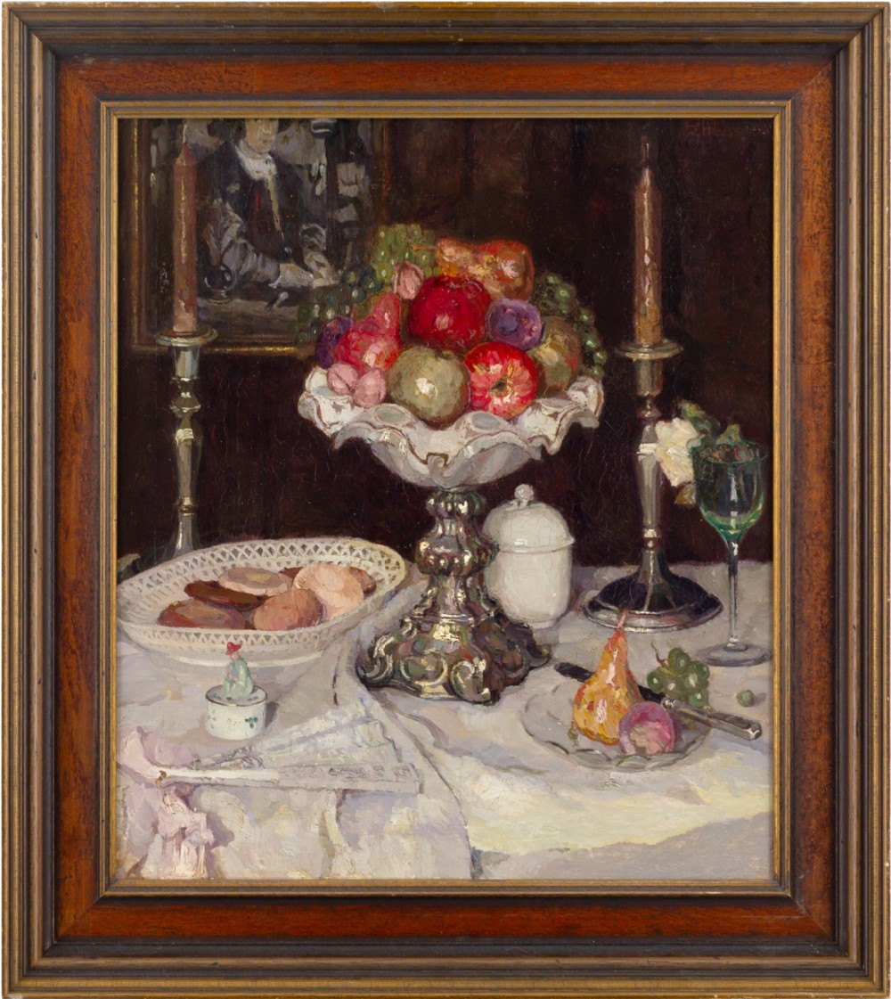 A framed oil painting featuring a tabletop still life arrangement of fruit, candlesticks, pastries, and glassware against a dark backdrop.