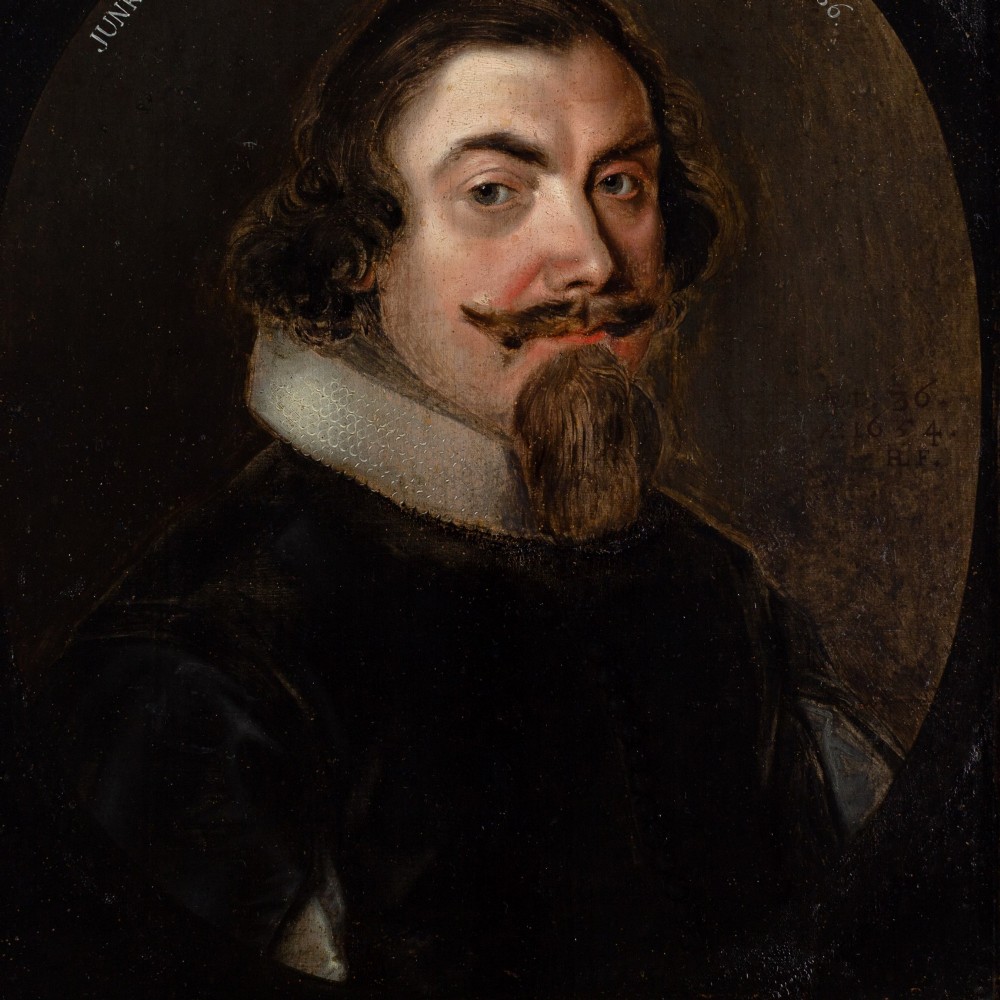 A 17th-century oil portrait depicting a gentleman with a pointed beard and white collar set within a painted oval spandrel and dark wooden frame. View VI