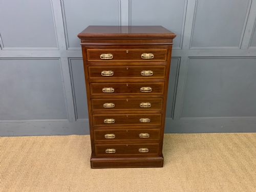 fig 1. A tall Edwardian mahogany pillar chest featuring seven inlaid drawers with brass drop handles on a plinth base.