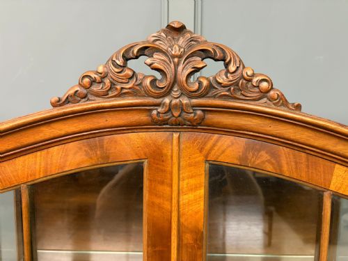 fig 3. An antique Queen Anne style glazed display cabinet in warm brown wood featuring arched doors with glass panes, drawers with brass handles, and carved cabriole legs.