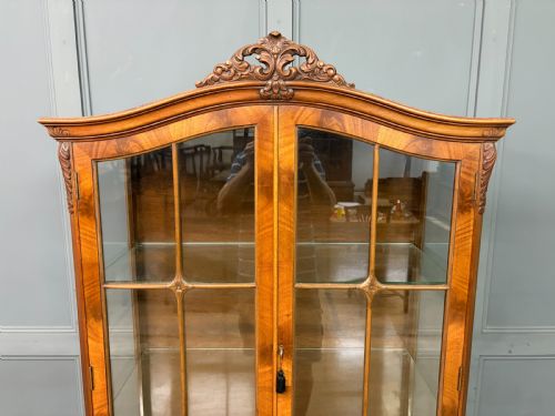 fig 4. An antique Queen Anne style glazed display cabinet in warm brown wood featuring arched doors with glass panes, drawers with brass handles, and carved cabriole legs.