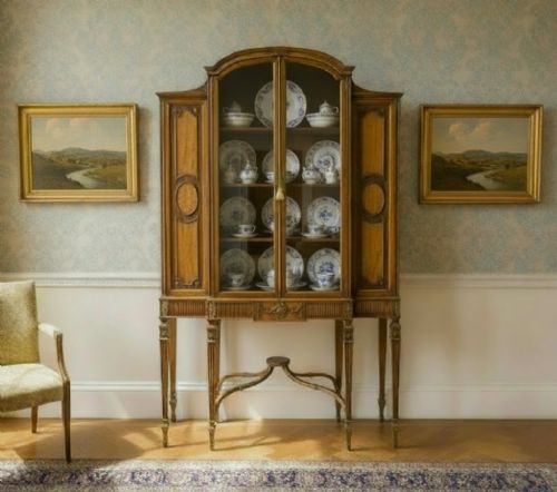 fig 1. A Neoclassical mahogany display cabinet featuring a central glazed door, flanking inlaid wood cupboards, and tapered fluted legs connected by an ornate curved stretcher.