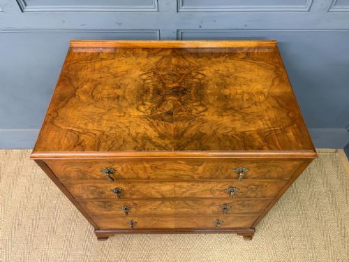 fig 3. An Art Deco burr walnut chest of four full-width drawers featuring figured veneer panels, decorative brass drop handles, and low bracket feet.