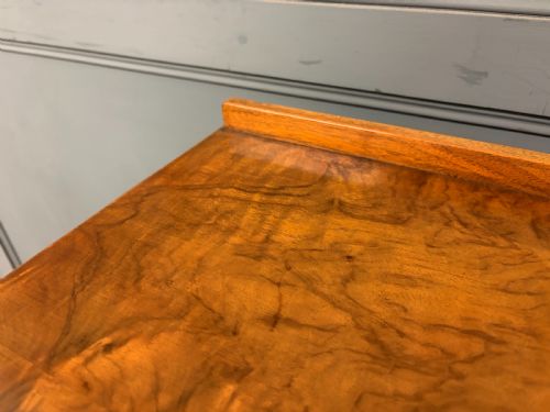 fig 4. An Art Deco burr walnut chest of four full-width drawers featuring figured veneer panels, decorative brass drop handles, and low bracket feet.