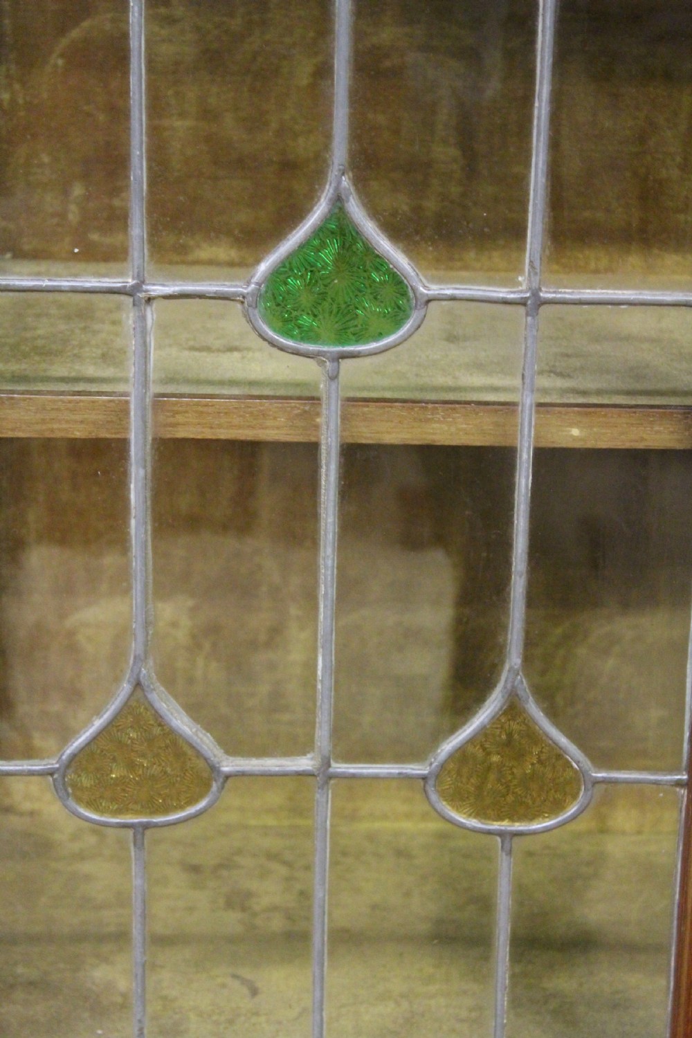 An Arts and Crafts inlaid mahogany display cabinet featuring leaded glass doors, a shaped gallery top with an oval mirror, and slender tapered legs. View V