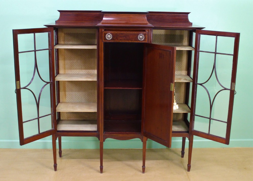 An Edwardian inlaid mahogany side cabinet featuring two outer glazed display doors, a central wooden door with an oval inlay panel, and square tapered legs. View II