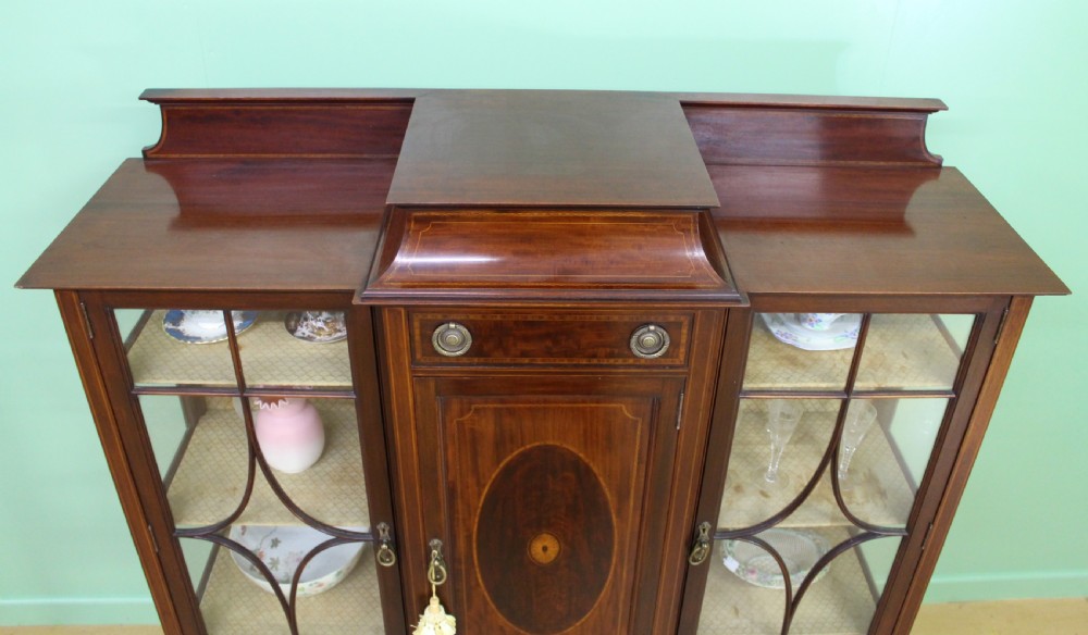 An Edwardian inlaid mahogany side cabinet featuring two outer glazed display doors, a central wooden door with an oval inlay panel, and square tapered legs. View III