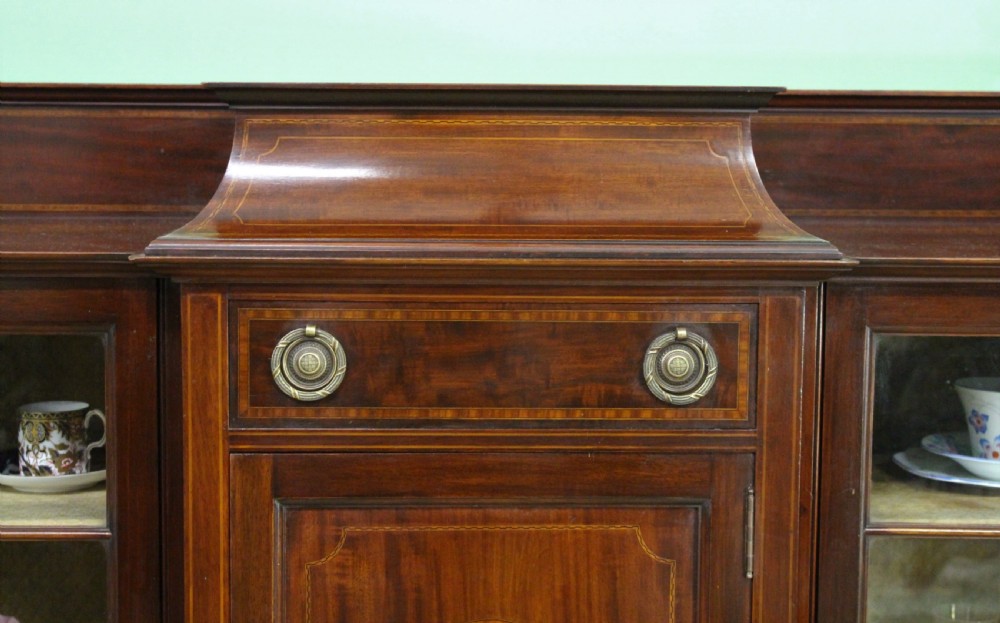 An Edwardian inlaid mahogany side cabinet featuring two outer glazed display doors, a central wooden door with an oval inlay panel, and square tapered legs. View VII