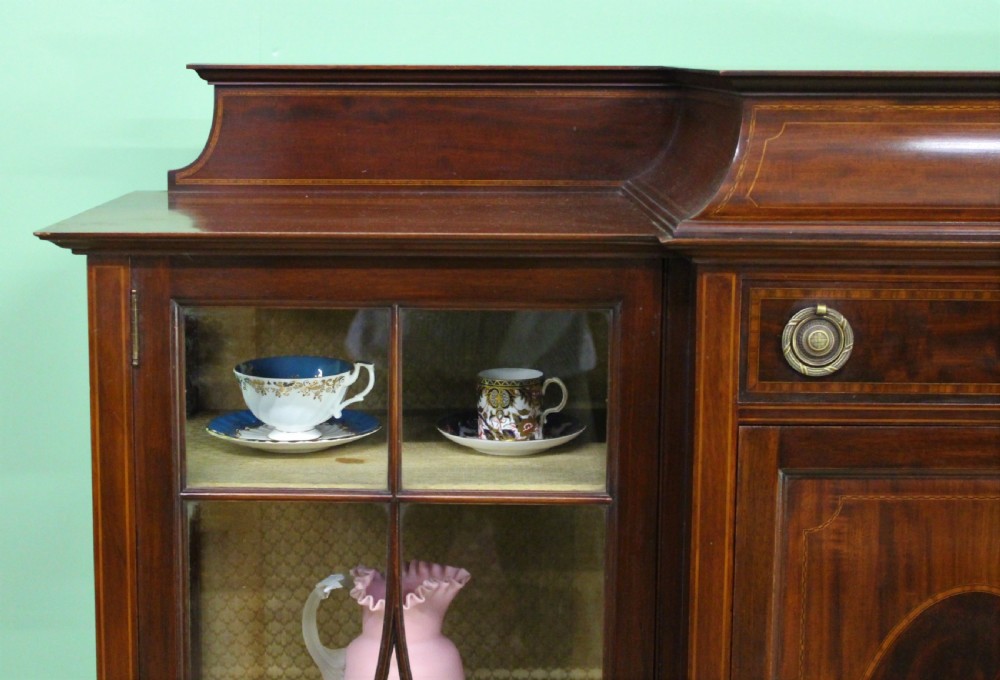 An Edwardian inlaid mahogany side cabinet featuring two outer glazed display doors, a central wooden door with an oval inlay panel, and square tapered legs. View IX