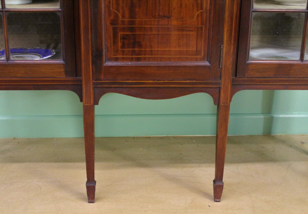 An Edwardian inlaid mahogany side cabinet featuring two outer glazed display doors, a central wooden door with an oval inlay panel, and square tapered legs. View X