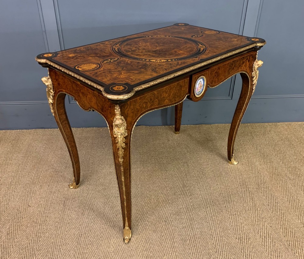 A 19th-century French burr walnut card table featuring intricate marquetry on the top, cabriole legs with gilt-bronze mounts, and a central porcelain plaque on the frieze.
