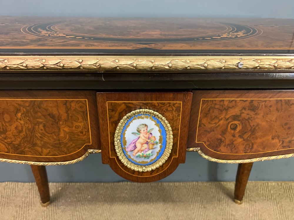 A 19th-century French burr walnut card table featuring intricate marquetry on the top, cabriole legs with gilt-bronze mounts, and a central porcelain plaque on the frieze. View IV
