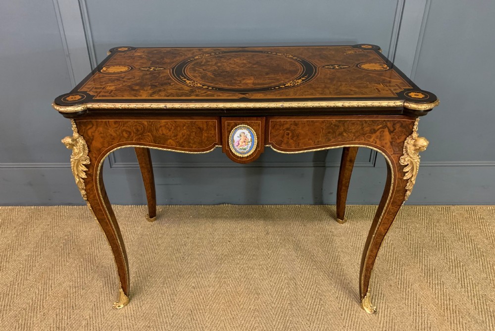 A 19th-century French burr walnut card table featuring intricate marquetry on the top, cabriole legs with gilt-bronze mounts, and a central porcelain plaque on the frieze. View V