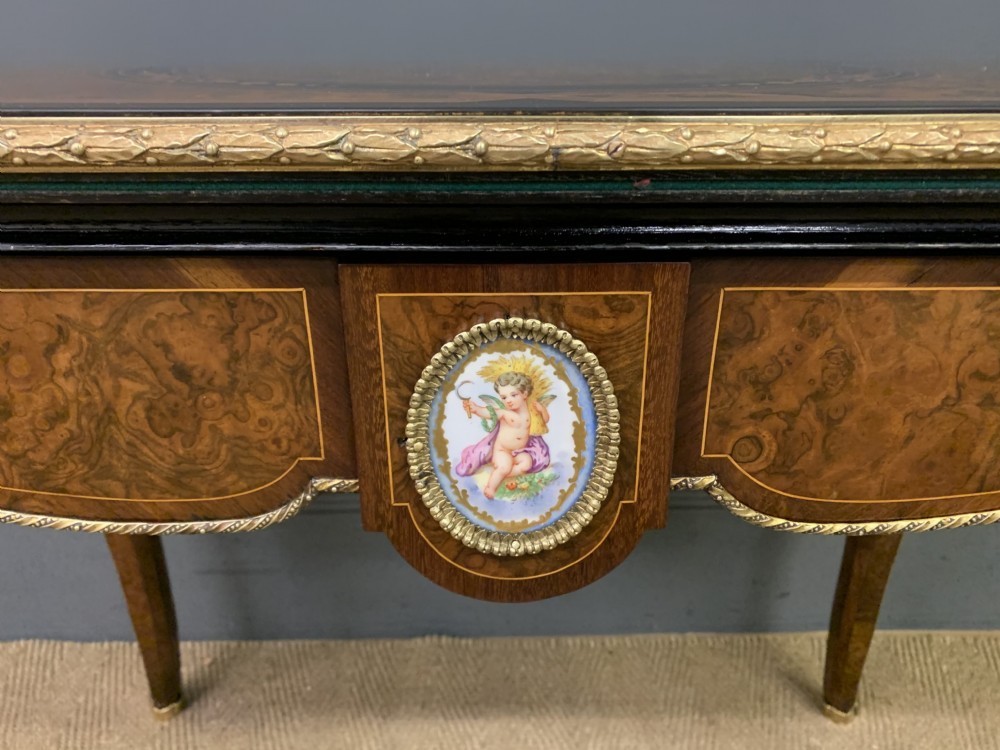 A 19th-century French burr walnut card table featuring intricate marquetry on the top, cabriole legs with gilt-bronze mounts, and a central porcelain plaque on the frieze. View XIV