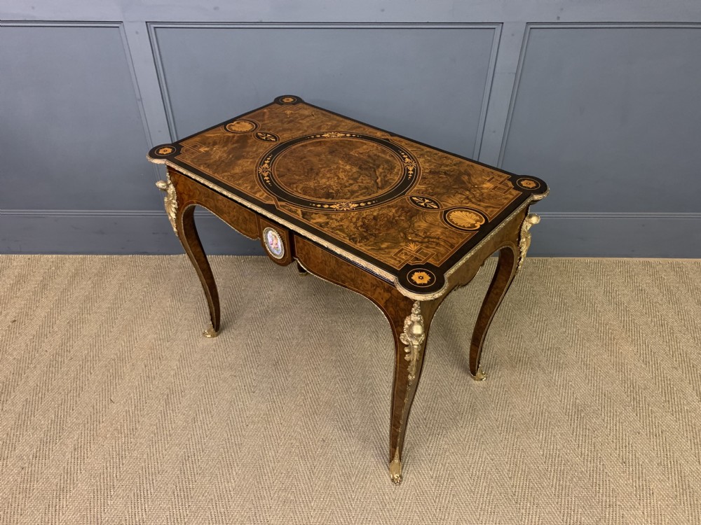 A 19th-century French burr walnut card table featuring intricate marquetry on the top, cabriole legs with gilt-bronze mounts, and a central porcelain plaque on the frieze. View XV