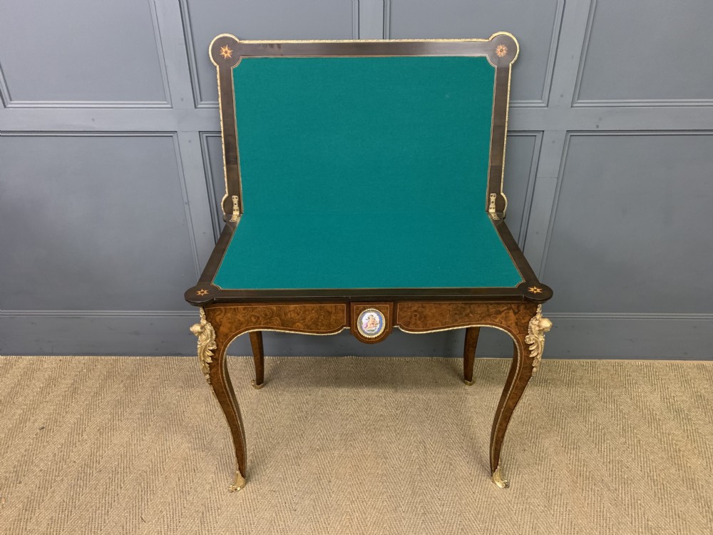 A 19th-century French burr walnut card table featuring intricate marquetry on the top, cabriole legs with gilt-bronze mounts, and a central porcelain plaque on the frieze. View XVI