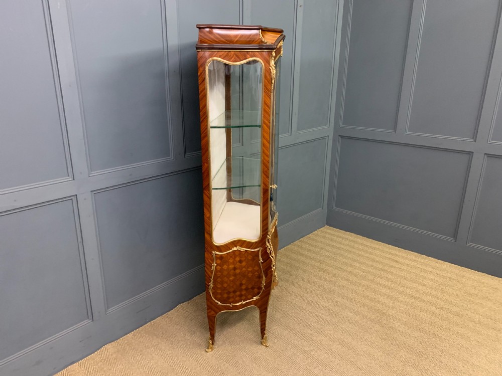 A 19th-century French kingwood vitrine cabinet with glass side panels, geometric parquetry lower door inlay, and ornate gilt-bronze ormolu mounts. View XII