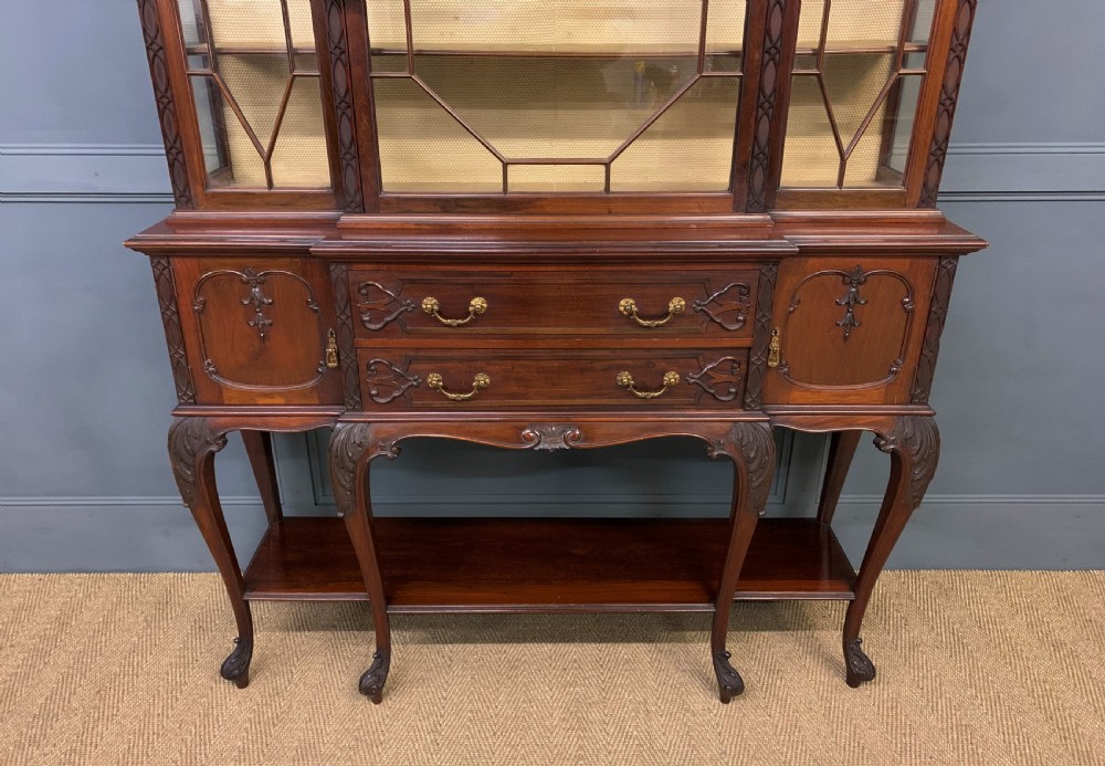 A carved dark mahogany display cabinet featuring three astragal glazed doors above drawers and cabriole legs on an undertier shelf. View III
