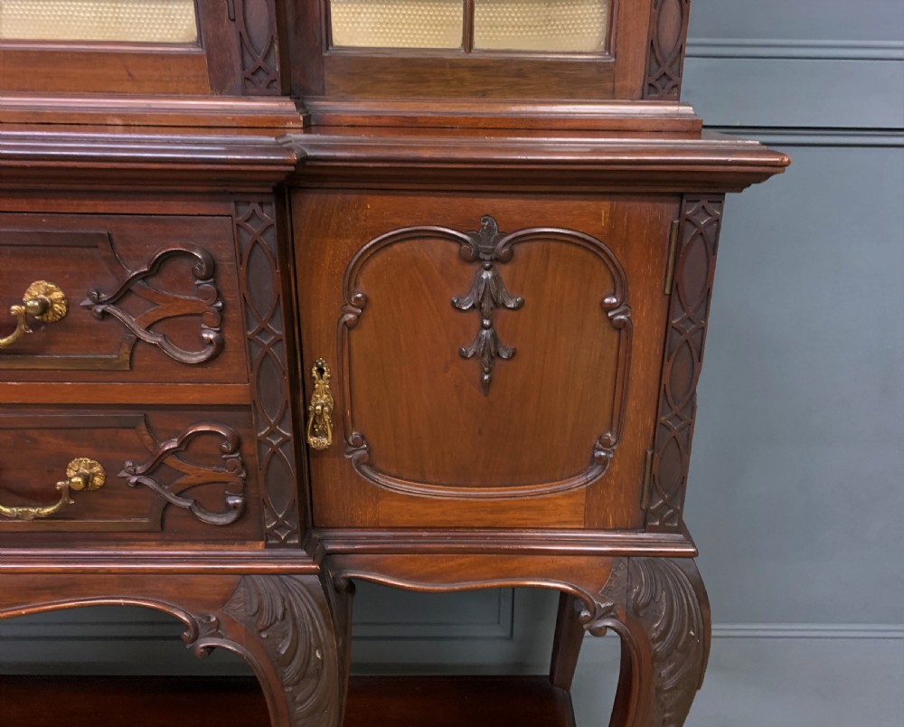 A carved dark mahogany display cabinet featuring three astragal glazed doors above drawers and cabriole legs on an undertier shelf. View VII