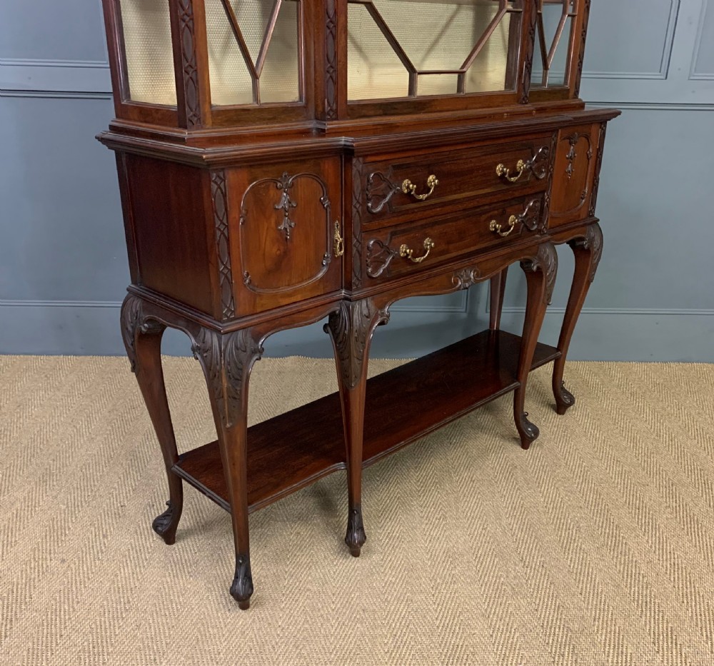 A carved dark mahogany display cabinet featuring three astragal glazed doors above drawers and cabriole legs on an undertier shelf. View XIII