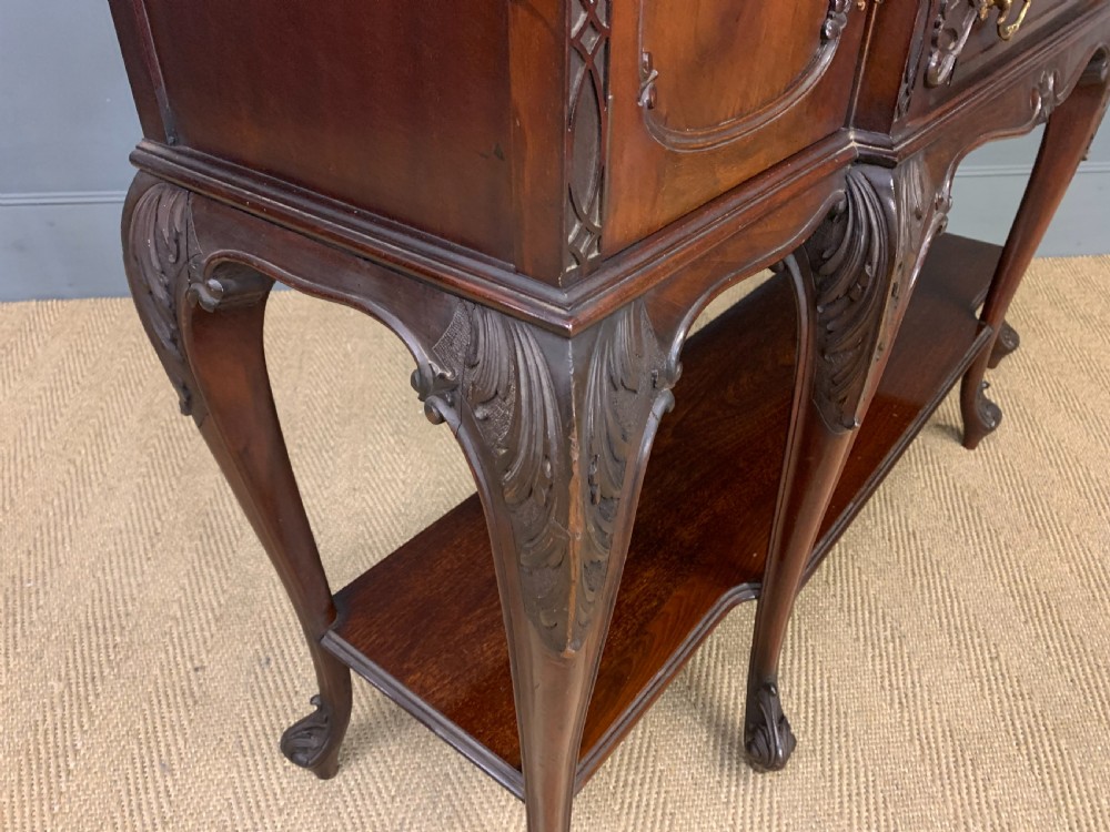 A carved dark mahogany display cabinet featuring three astragal glazed doors above drawers and cabriole legs on an undertier shelf. View XV