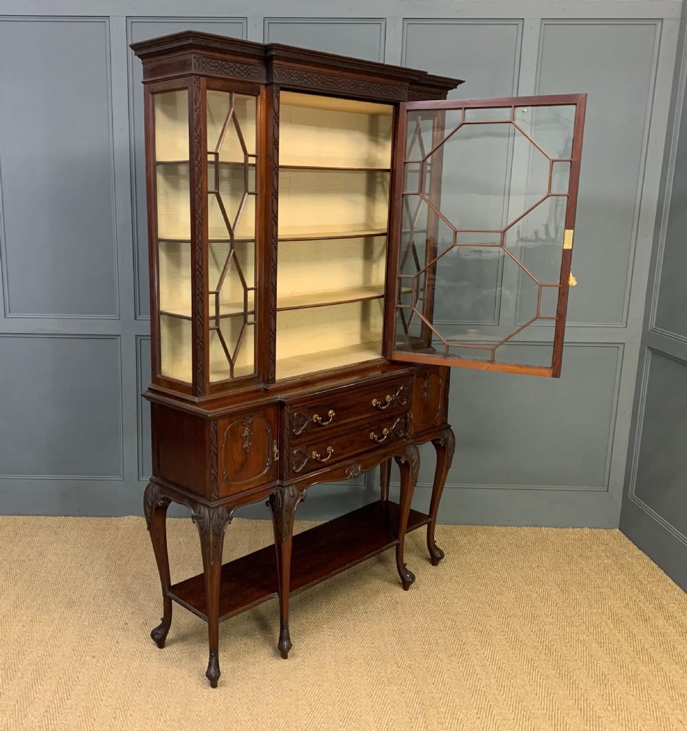 A carved dark mahogany display cabinet featuring three astragal glazed doors above drawers and cabriole legs on an undertier shelf. View XVI