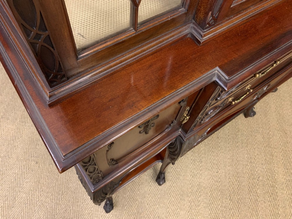 A carved dark mahogany display cabinet featuring three astragal glazed doors above drawers and cabriole legs on an undertier shelf. View XVII