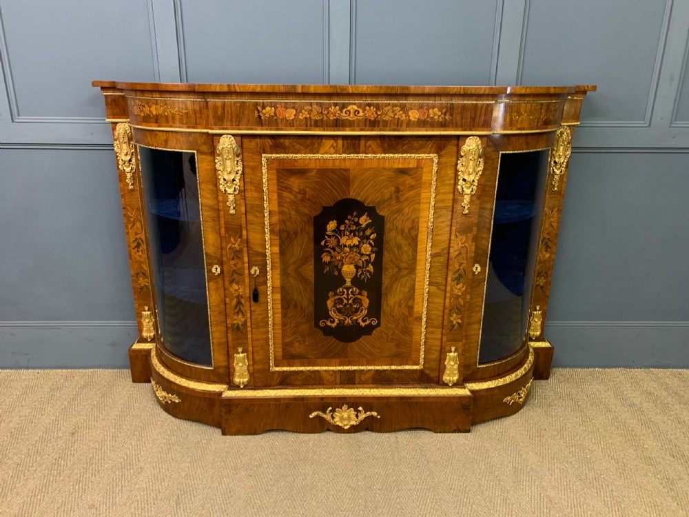 A Victorian burr walnut credenza featuring floral marquetry inlays, gilt bronze ormolu mounts, a central panelled door, and curved glazed side cabinets. View II