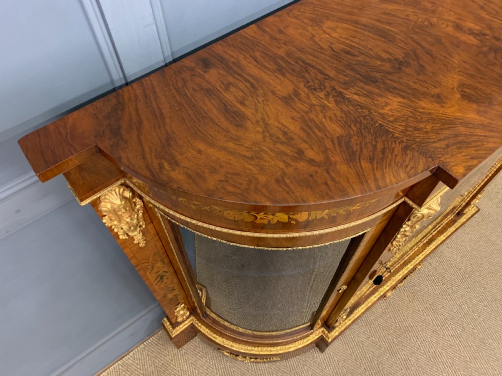 A Victorian burr walnut credenza featuring floral marquetry inlays, gilt bronze ormolu mounts, a central panelled door, and curved glazed side cabinets. View IV