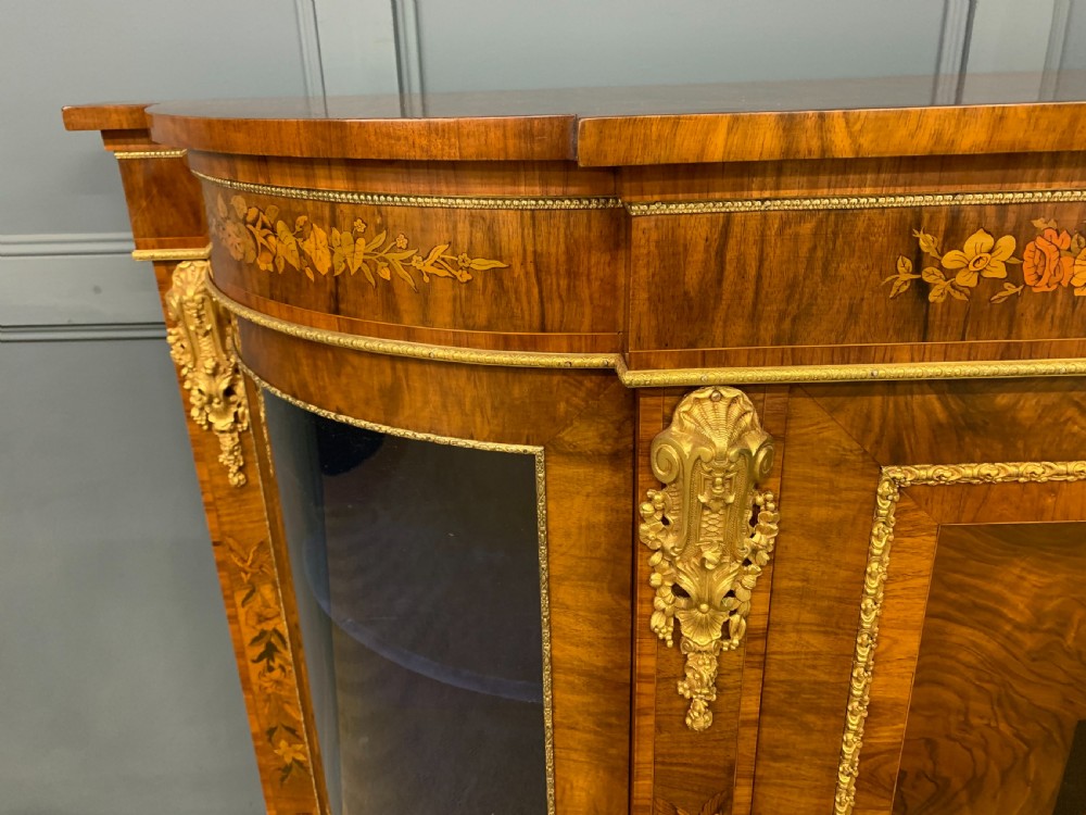 A Victorian burr walnut credenza featuring floral marquetry inlays, gilt bronze ormolu mounts, a central panelled door, and curved glazed side cabinets. View V