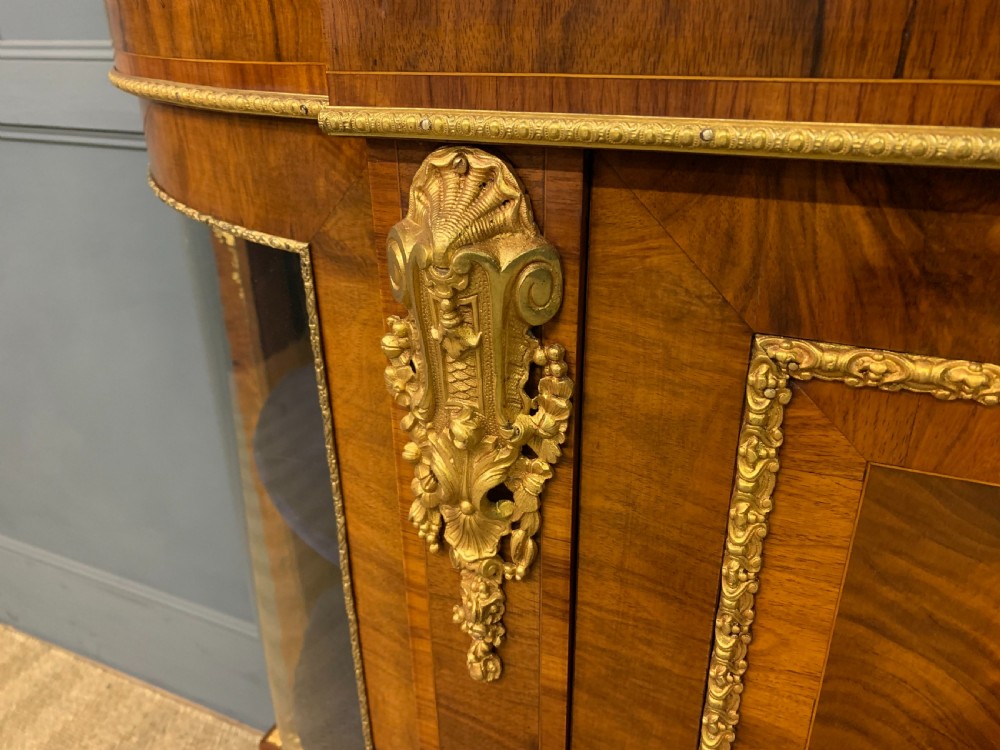 A Victorian burr walnut credenza featuring floral marquetry inlays, gilt bronze ormolu mounts, a central panelled door, and curved glazed side cabinets. View VI