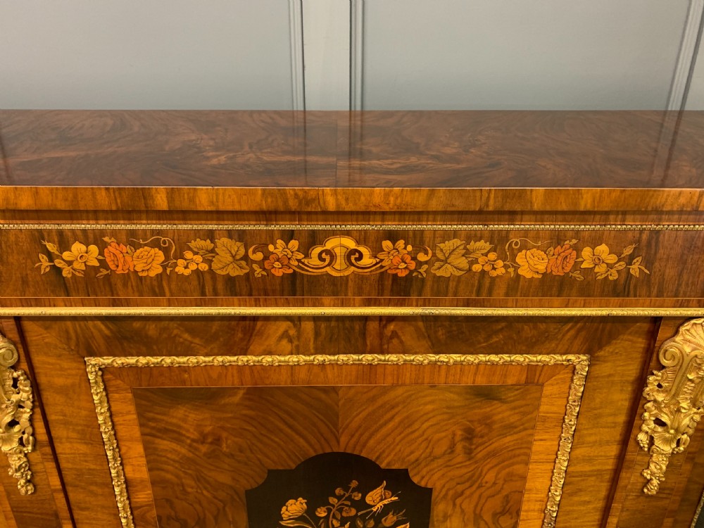 A Victorian burr walnut credenza featuring floral marquetry inlays, gilt bronze ormolu mounts, a central panelled door, and curved glazed side cabinets. View VII