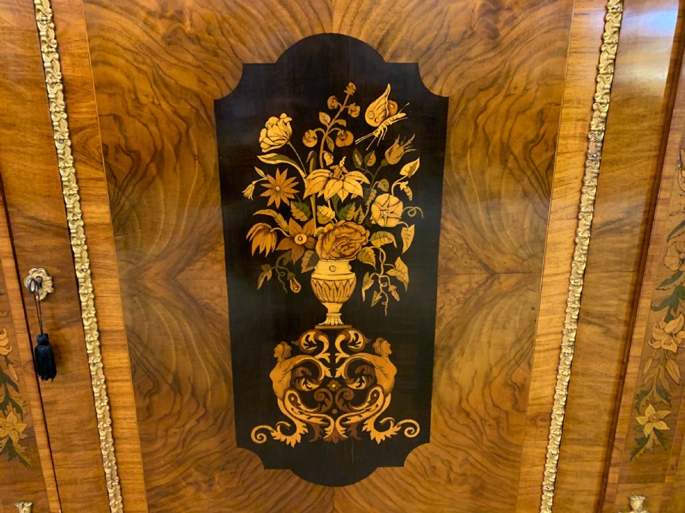 A Victorian burr walnut credenza featuring floral marquetry inlays, gilt bronze ormolu mounts, a central panelled door, and curved glazed side cabinets. View X
